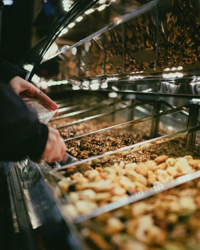 Hands selecting nuts and dried fruits from market display. Indoor lighting, close-up view.