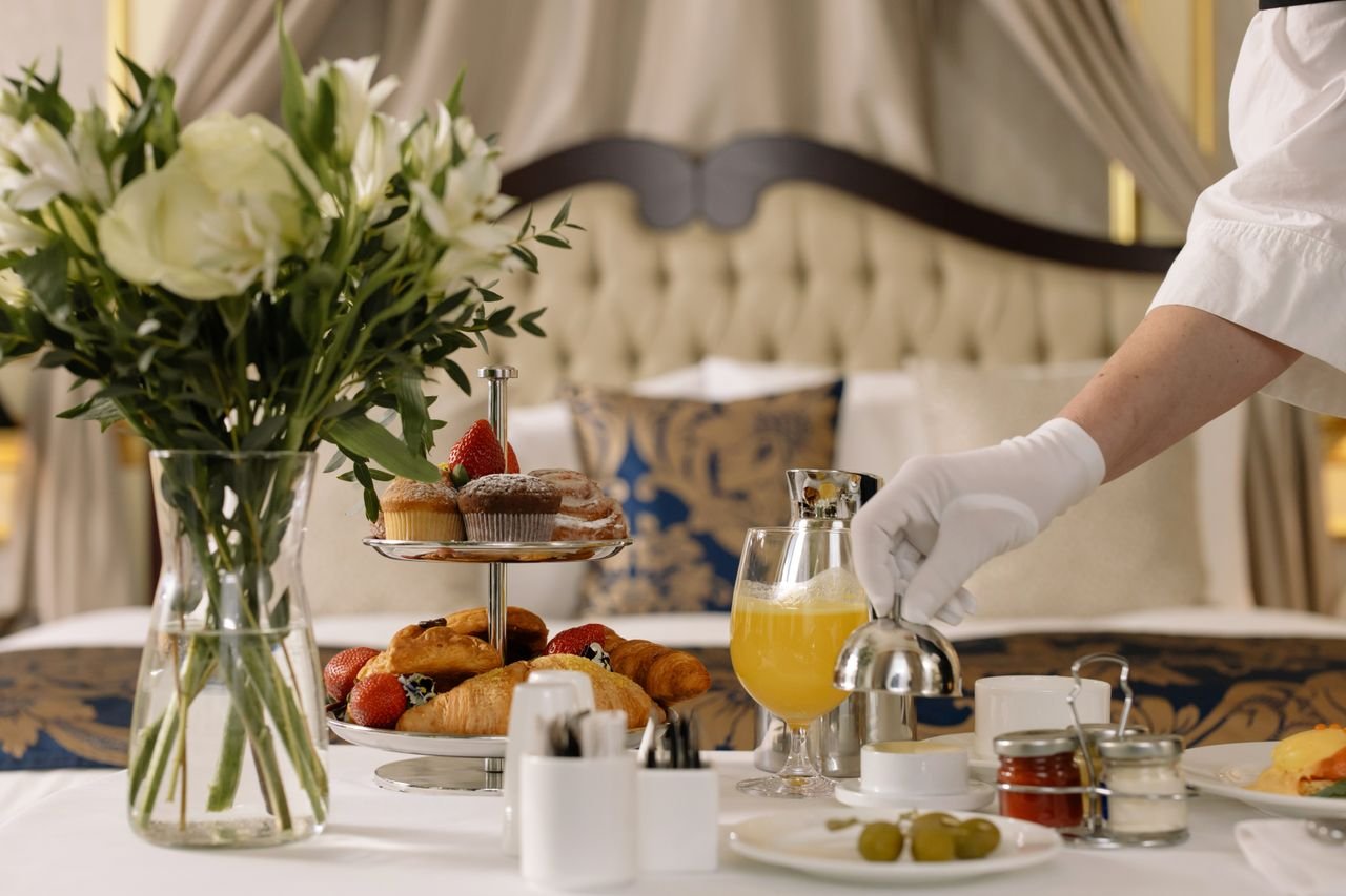 Luxurious hotel room service with pastries, juice, and fresh flowers on a table.
